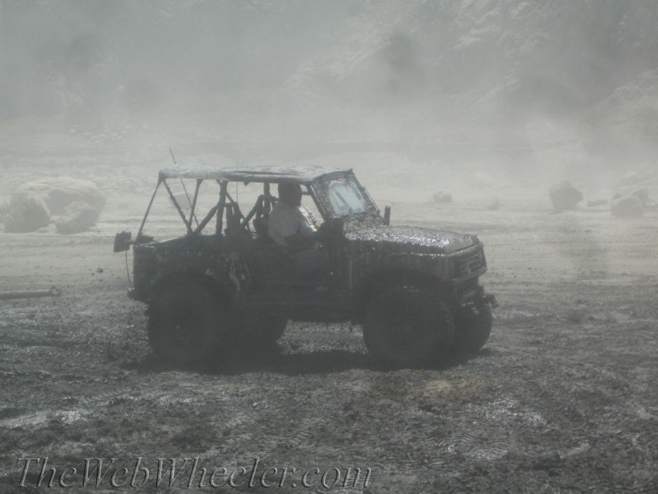 Muddy off-road vehicle driving through a muddy area. Driver is visible inside