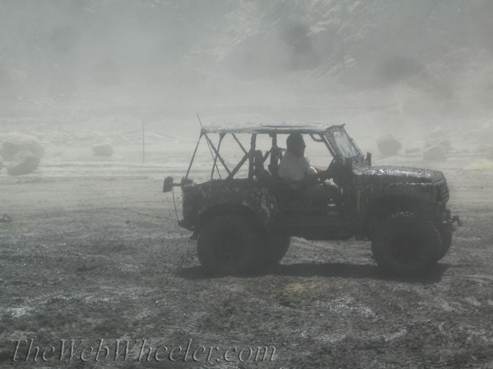Mud-covered off-road vehicle with a roll cage driving through a muddy field
