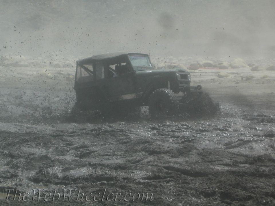 1987 Suzuki Samurai driving through mud, kicking up spray