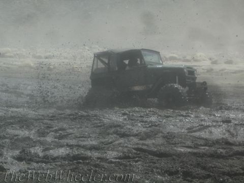 1987 Suzuki Samurai - An off-road vehicle navigates a muddy terrain, kicking up a large spray.