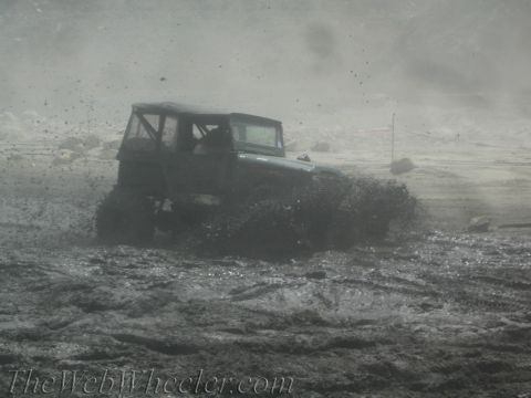 1987 Suzuki Samurai - A dark off-road vehicle navigates through a muddy terrain, kicking up spray.