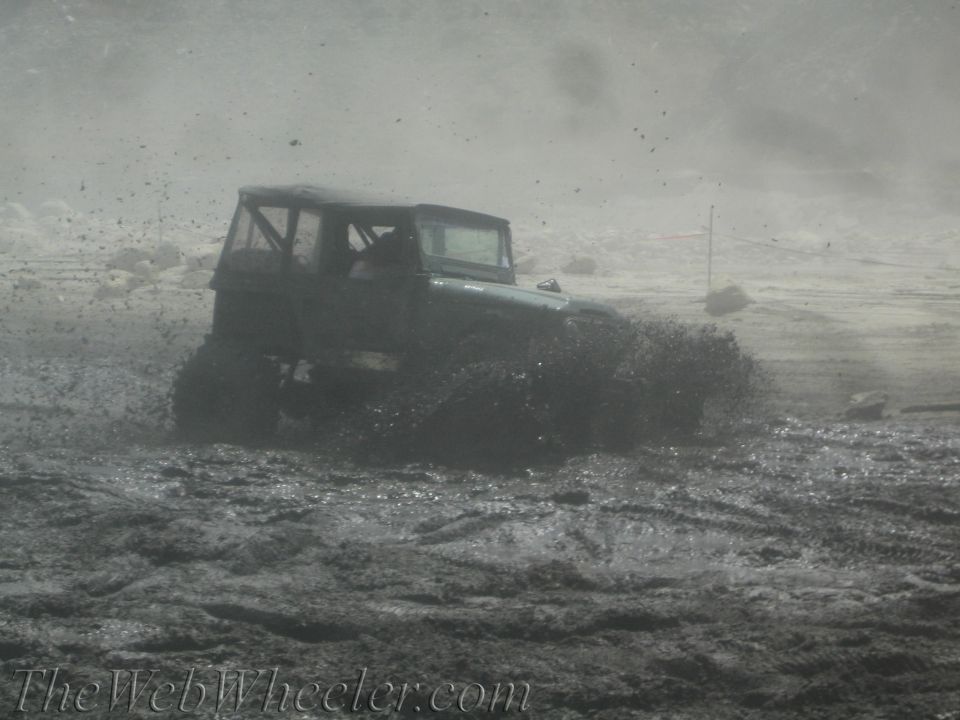 Dark off-road vehicle splashing through mud, low angle