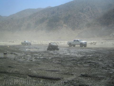 1987 Suzuki Samurai - Several trucks are navigating a muddy, dusty terrain with hills in the distance.
