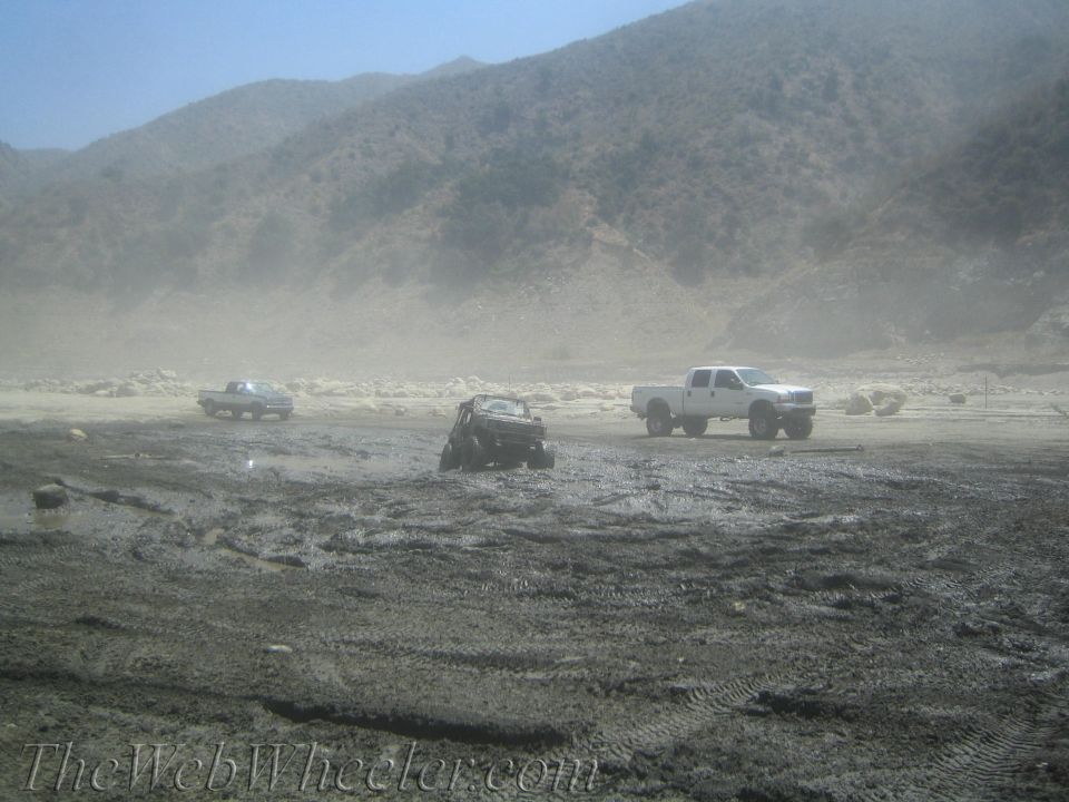 three trucks in a muddy, dusty area with hills in the background