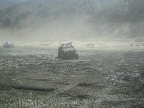 1987 Suzuki Samurai - An off-road vehicle is stuck in a muddy landscape, with another vehicle visible in the distance under hazy skies.