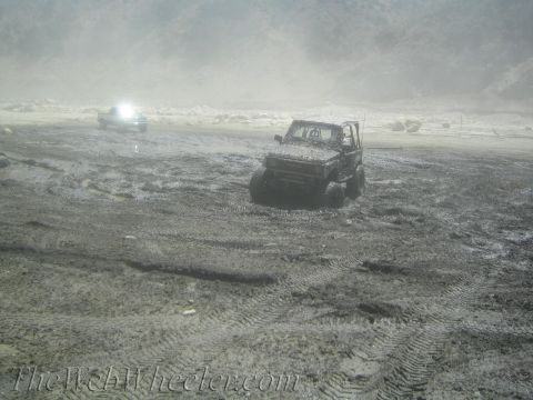 1987 Suzuki Samurai - Two off-road vehicles are stuck in a muddy, desolate landscape under a hazy sky.