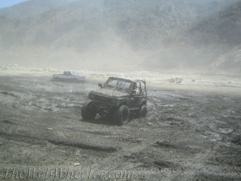 1987 Suzuki Samurai - A muddy Suzuki Samurai navigates a treacherous off-road terrain with a pickup truck in the distance.