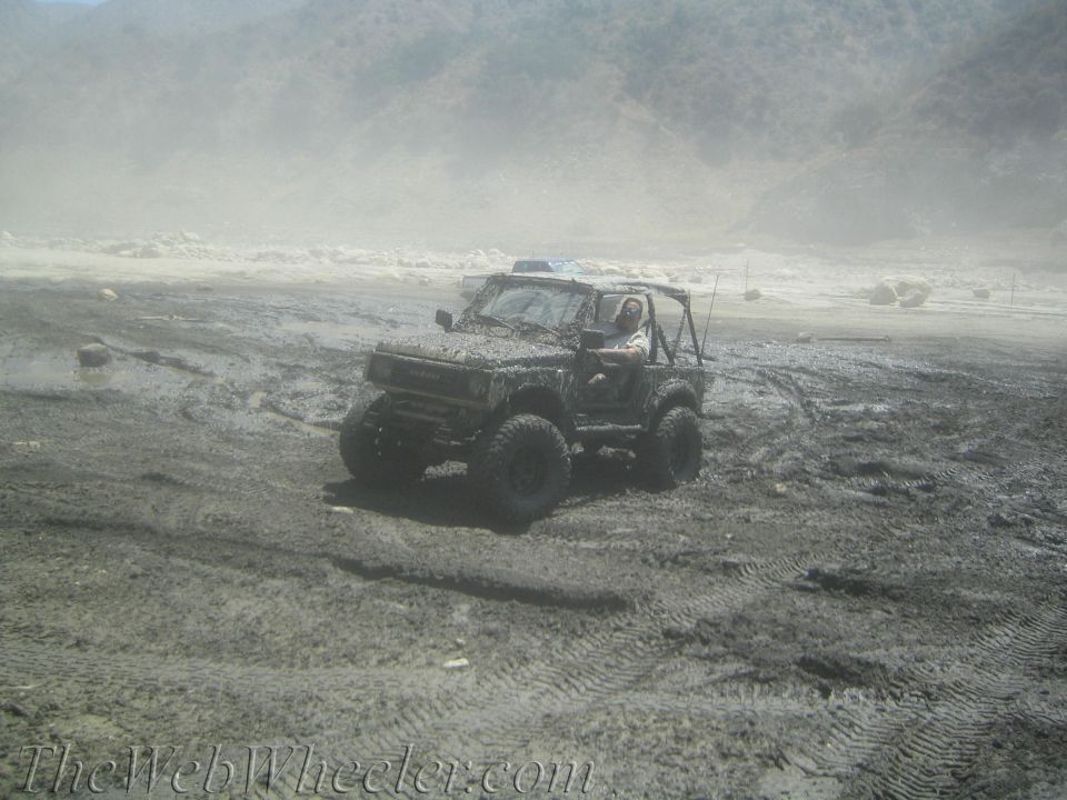 1987 Suzuki Samurai covered in mud, stuck in a muddy field with tire tracks visible