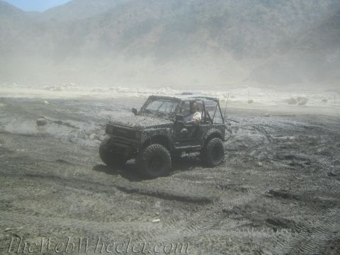 1987 Suzuki Samurai - A Suzuki Samurai navigates a muddy terrain, kicking up dust and spray.