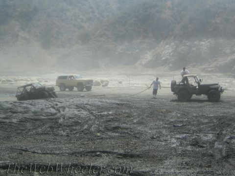 1987 Suzuki Samurai - Several off-road vehicles are stuck in thick mud, with people attempting to pull them out with a rope.