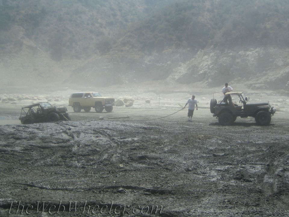 Three off-road vehicles stuck in mud, two people pulling a rope