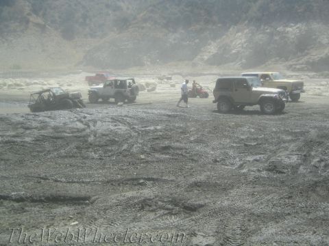 1987 Suzuki Samurai - Several off-road vehicles are gathered on a muddy terrain with hills in the background.