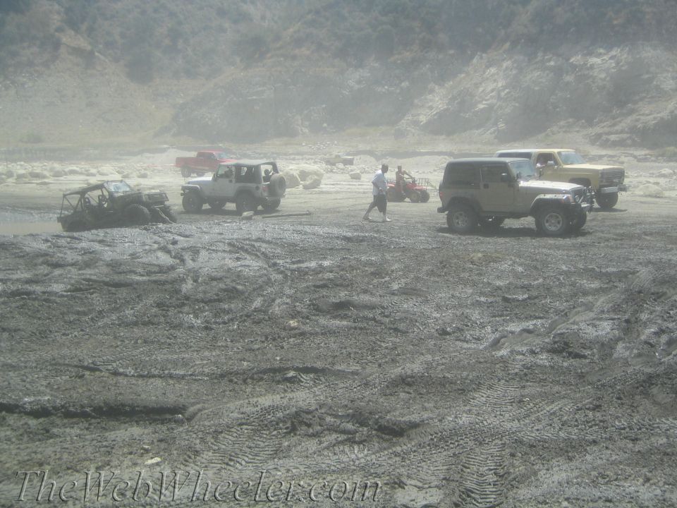 Tan Jeep Wrangler parked on muddy ground with other off-road vehicles and people in the background
