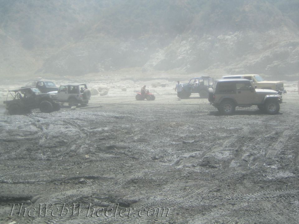 Several off-road vehicles parked on dusty ground with hills in the background