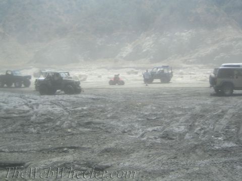 1987 Suzuki Samurai - A group of off-road vehicles and an ATV are gathered in a dusty, outdoor area with hills in the distance.