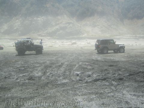 1987 Suzuki Samurai - Two off-road vehicles are stuck in a muddy, sandy terrain with hills in the background.