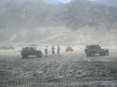 1987 Suzuki Samurai - A group of off-road vehicles and ATVs are gathered in a dusty, arid environment, with mountains dominating the horizon.