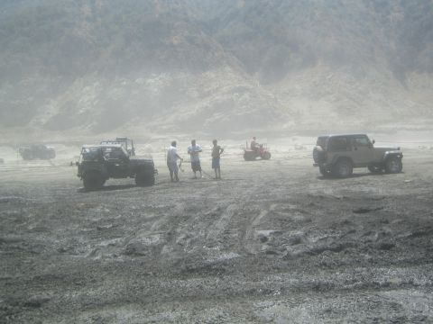 1987 Suzuki Samurai - Off-road vehicles and people in a dusty, barren landscape with hills in the distance.