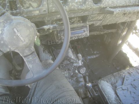 1987 Suzuki Samurai - The interior of a 1987 Suzuki Samurai is heavily covered in mud, obscuring most details except for the steering wheel and gear shift.