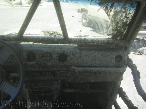 1987 Suzuki Samurai - The interior of a mud-caked 1987 Suzuki Samurai shows a roll cage and dashboard, with another vehicle visible through the windshield.