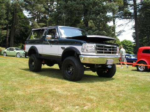1994 Ford Bronco - A lifted Ford Bronco is displayed outdoors with its hood up, alongside other vehicles.