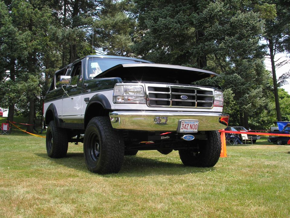 Two-tone green and white Ford Bronco with hood open, lifted suspension, and aftermarket wheels