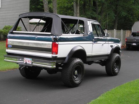 1994 Ford Bronco - A lifted Ford Bronco with a removable soft top is parked on a driveway, with another truck in the background.