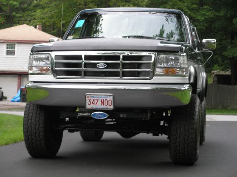 1994 Ford Bronco - A lifted Ford Bronco is parked on a paved surface, showing its front grille and tires.