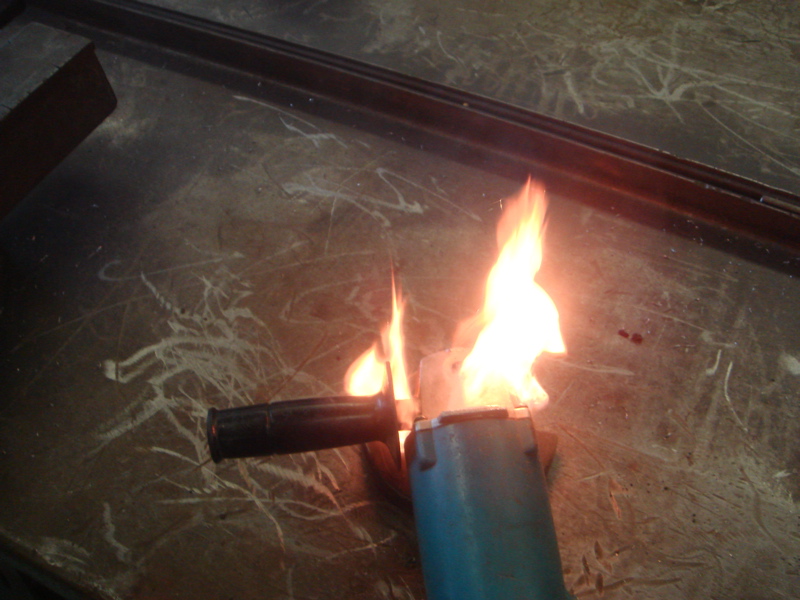 Angle grinder with flames coming out of it, sitting on a scratched surface