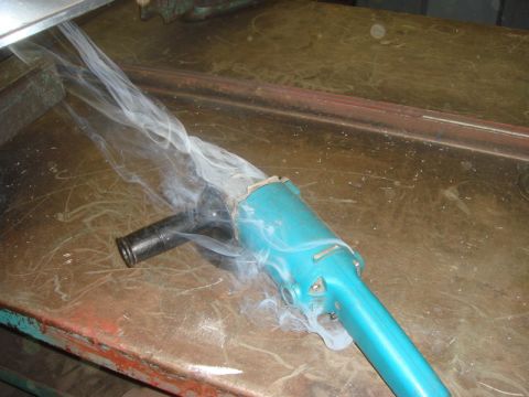 1996 Ford Bronco - A grinder appears to be malfunctioning, emitting smoke from its connection to a hose on a cluttered workbench.