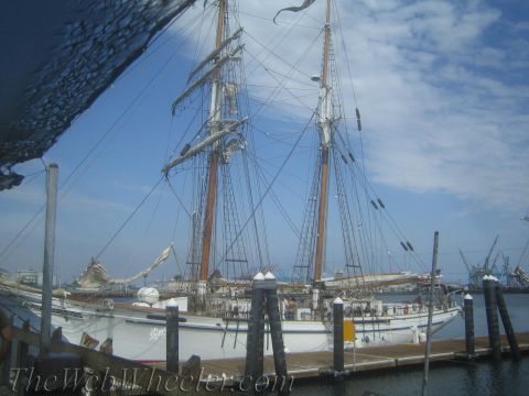 1990 Ford Bronco - two-masted tall ship with furled sails sits moored at a harbor dock beneath a partly cloudy blue sky.