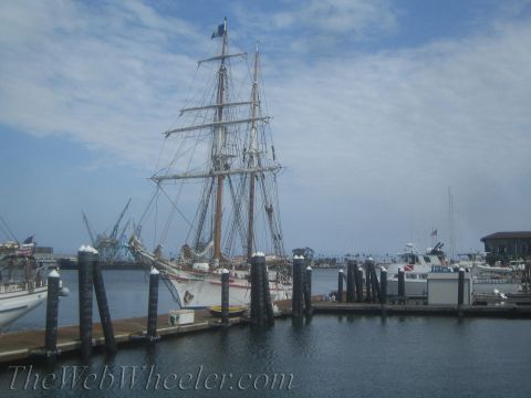 1990 Ford Bronco - masted tall ship rests among smaller boats at a harbor marina with industrial cranes on the far shore.