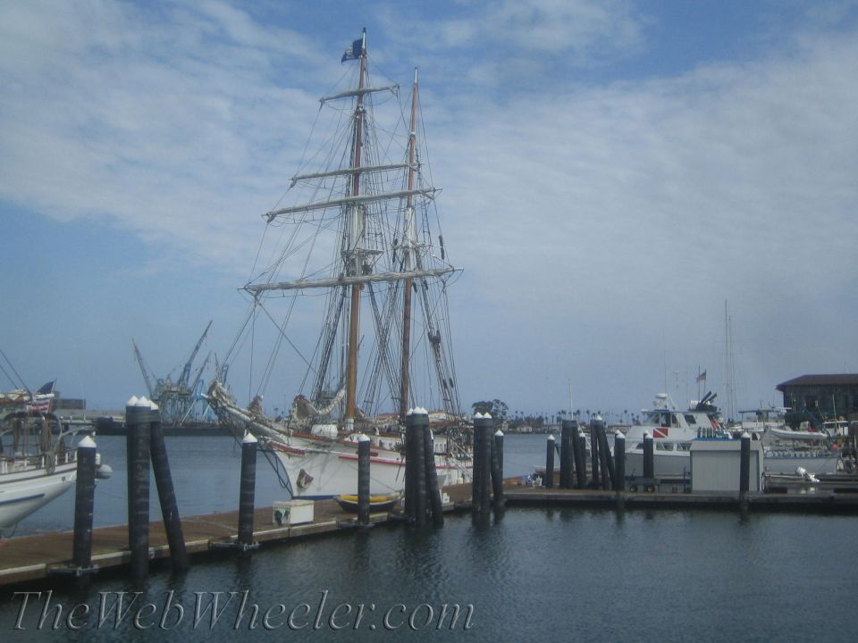 Tall ship and other boats moored at a harbor with cranes in the distance