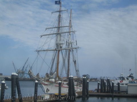 1990 Ford Bronco - tall sailing ship with carved bow figureheads sits docked at a marina with other vessels and harbor cranes behind.