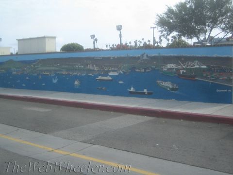 1990 Ford Bronco - long blue mural depicting a busy harbor scene with ships and boats stretches along a roadside wall above the curb.