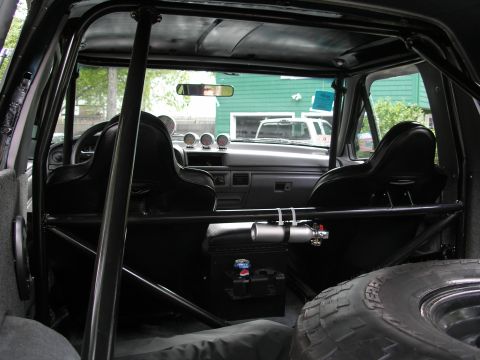1994 Ford Bronco - The interior of a heavily modified SUV features racing seats and a full roll cage, with another vehicle visible outside.