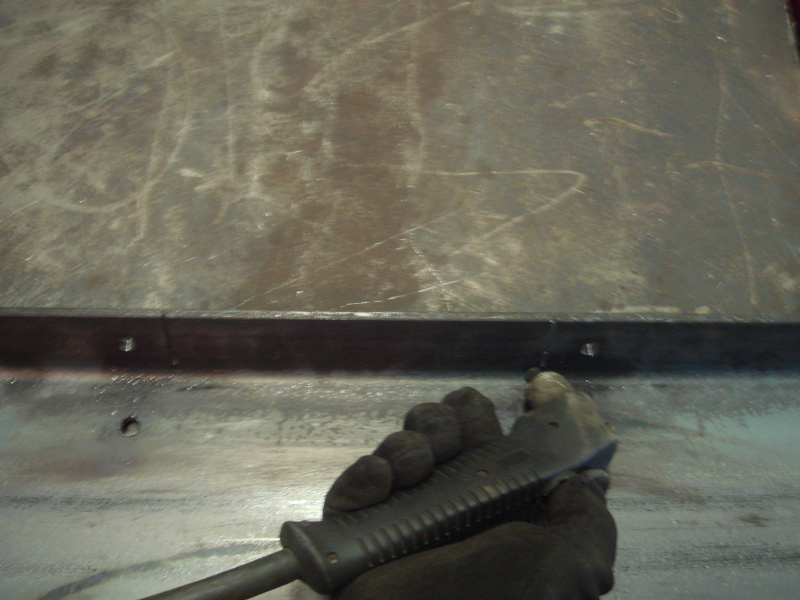 Gloved hand holding a tool against a metal surface