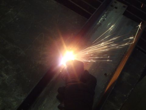 1996 Ford Bronco - A close-up shot shows a gloved hand holding a welding torch, emitting a shower of bright sparks against a dark background.