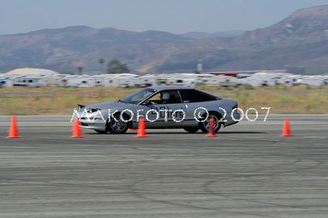 1993 Ford Probe - A silver coupe is seen on an asphalt track, maneuvering around orange cones during a timed event.