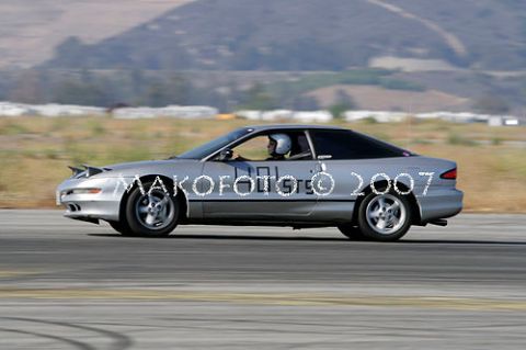1993 Ford Probe - A silver coupe is seen in profile on a race track, with racing numbers visible on its side.