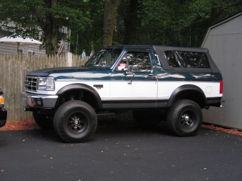 1994 Ford Bronco - Side view of a lifted 1994 Ford Bronco with a two-tone paint scheme and a removable soft top.