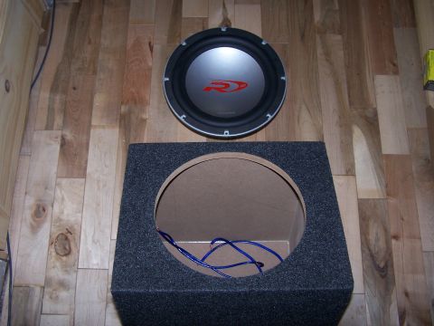 1995 Ford Probe - A car subwoofer and its enclosure are shown on a wooden floor.