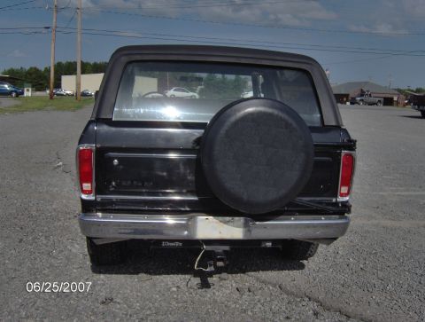 1978 Ford Bronco - The rear of a black Ford Bronco is shown with a spare tire on the tailgate and a trailer hitch below the bumper.