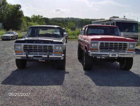 1978 Ford Bronco - Two Ford Broncos are parked side-by-side on a gravel lot, with an RV visible in the background.