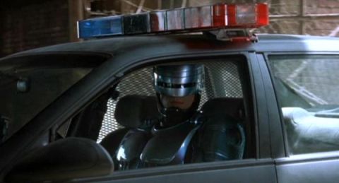 2000 Ford Crown Victoria - A person in a robotic suit sits in the driver's seat of a police car.