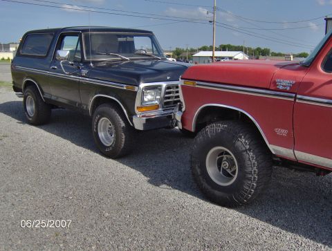 1978 Ford Bronco - Two Ford Broncos are parked side-by-side on a gravel lot under a partly cloudy sky.