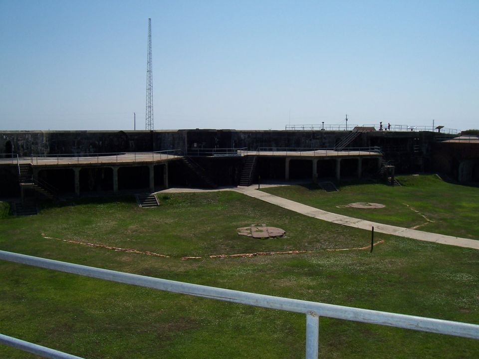 view of a large stone fort with a central grassy area and walkways, under a clear blue sky