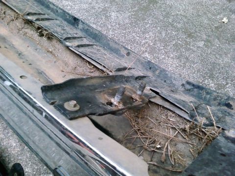 1995 Ford Bronco - Close-up of a chrome bumper section showing a mounting bracket with bolts, covered in dirt and grass.