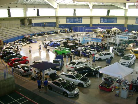 1975 Ford Bronco - Many cars are on display at an indoor automotive event, with spectators walking around.