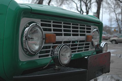1975 Ford Bronco - Close-up of a green Ford Bronco's front grille, showing its distinctive design and headlights.